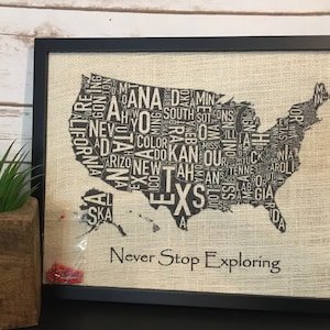 May include: A framed burlap print of a map of the United States. The map is made up of the names of all the states. The text "Never Stop Exploring" is printed below the map.