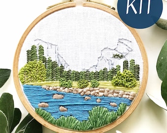 May include: A DIY embroidery kit featuring a scenic landscape with mountains, trees, and a river. The kit includes a hoop, fabric, and embroidery floss.