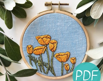 May include: Embroidered hoop art featuring a cluster of yellow California poppies on a light blue background. The hoop is made of wood and has a brass screw.