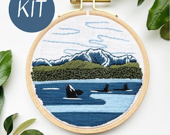 May include: Embroidered hoop art kit featuring a scenic landscape with mountains, trees, and orcas swimming in the water. The kit includes all the materials needed to complete the project.