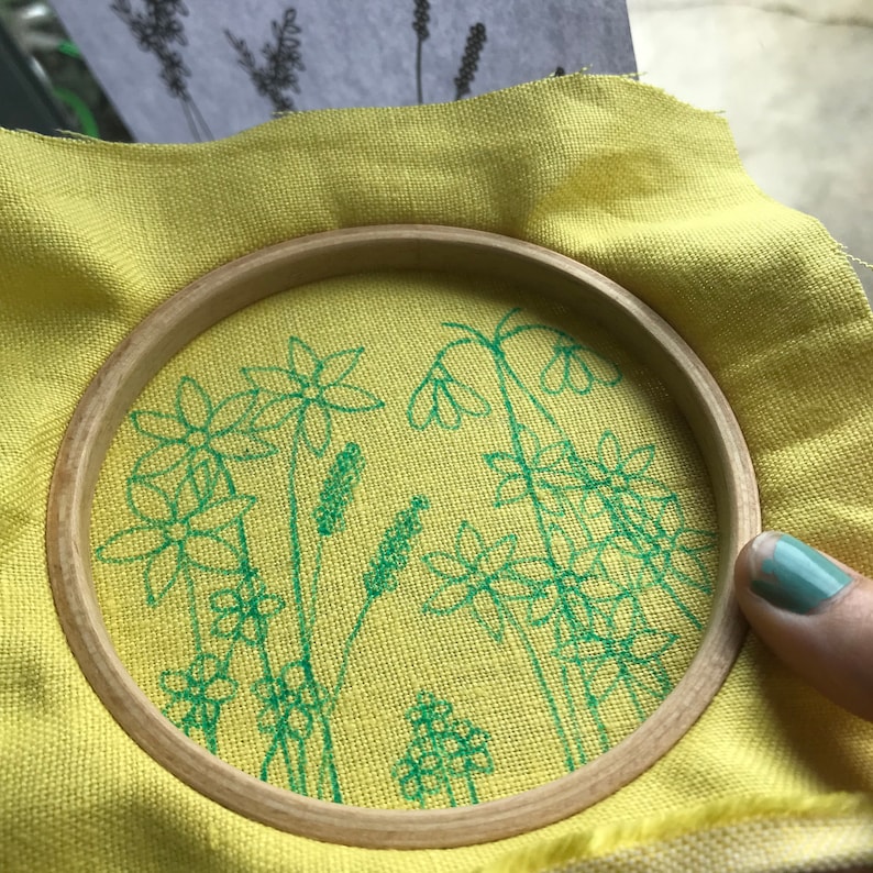 Start by transferring your desired flowers to the fabric by holding it tight in a hoop in front of a sunny window.