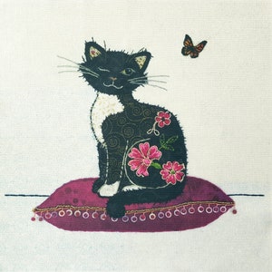May include: A black and white cat with pink flowers embroidered on its back sits on a burgundy pillow with gold trim. A small orange butterfly is flying above the cat.