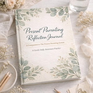 May include: A hardcover journal titled "Present Parenting Reflection Journal" with a floral design. The cover features the title in elegant script and botanical illustrations. The journal is accompanied by pencils, paper clips, and a glass of water, suggesting a workspace.