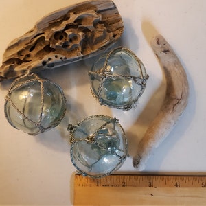 May include: Three glass fishing floats with a net-like design, two pieces of driftwood, and a wooden ruler.