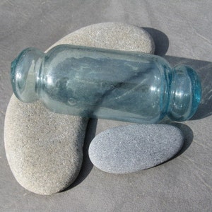 May include: A light blue glass bottle with a rounded bottom and a slightly flared top, resting on two gray stones.