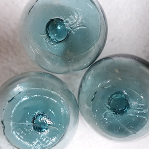 May include: Three blue glass fishing floats with a white background. The floats are round and have a small hole in the center.