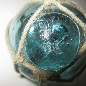 May include: A blue glass fishing float with a rope net and the letters "J.L." embossed on the surface.