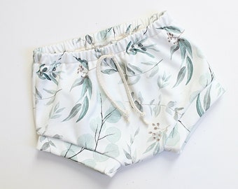 May include: White baby bloomers with a green and brown leafy print. The bloomers have a drawstring waist.
