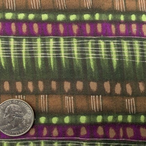 May include: A close-up of a fabric with a repeating pattern of brown, green, and purple stripes. The fabric has a textured surface and a subtle sheen. A US quarter is placed on the fabric for scale.