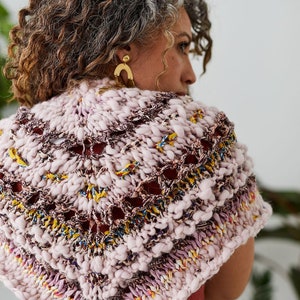 May include: A pink and purple knitted shawl with a lacy pattern. The shawl is made with a chunky yarn and has a textured look.
