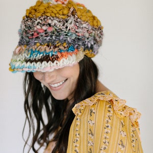 May include: A woman wearing a colourful knitted hat with a wide brim and a yellow floral patterned blouse.