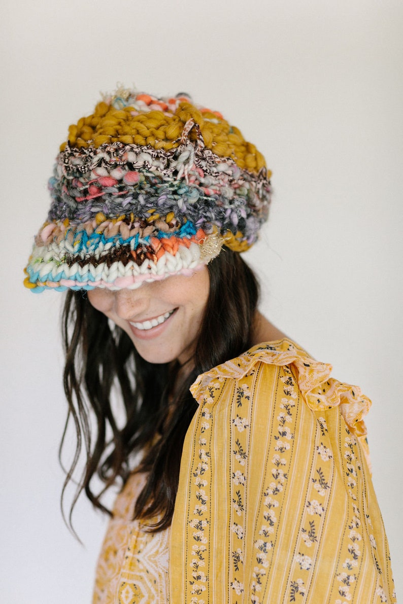 May include: A woman wearing a colorful knitted hat with a wide brim and a yellow floral patterned blouse.