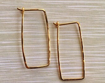 Könnte beinhalten: Ein Paar goldfarbene rechteckige Creolen. Die Ohrringe sind aus dünnem Metall gefertigt und haben eine leicht gehämmerte Textur.