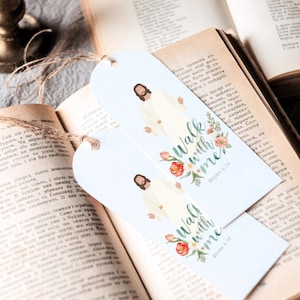 Könnte beinhalten: Zwei weiße Lesezeichen mit dem Text "Walk with me" und einer Abbildung von Jesus. Die Lesezeichen haben ein Blumendesign mit roten und rosa Blumen. Sie liegen auf einem offenen Buch.