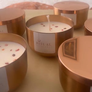 May include: Four gold candle jars with lids. The candle jars have white wax with red flecks and a white wick. The label on the front of the candle jar reads "Ritual Abundance".
