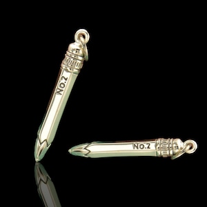 May include: Two silver pencil charms with a detailed design and the inscription "NO.2" on each. The charms are on a black background.