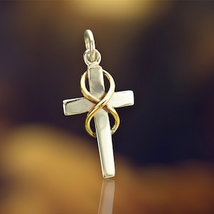 Puede incluir: Un colgante de cruz de plata con un símbolo de infinito de oro envuelto alrededor. El colgante está sobre un fondo borroso.
