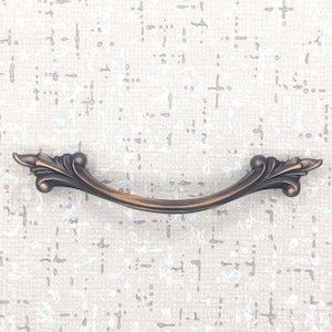 May include: A white ceramic mug with a black handle and the text "But First, Coffee" in a bold, black font. The mug is set against a blurred background, suggesting a cosy setting.