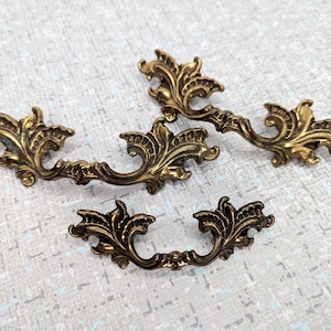 May include: Three ornate brass drawer pulls with a floral design. The pulls have a vintage look and would be a great addition to any home decor project.