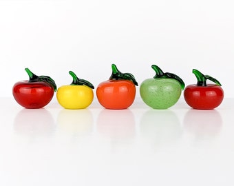May include: Five colorful glass apple figurines. The apples are red, yellow, orange, green, and red. Each apple has a green stem and leaf. The figurines are arranged in a row against a white background.