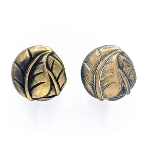 May include: Two round, gold-toned cabinet knobs with a leaf design. The knobs have a distressed finish.
