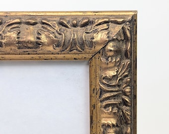 May include: Close-up of the corner of a gold picture frame with ornate detailing. The frame has a distressed finish and a raised design.