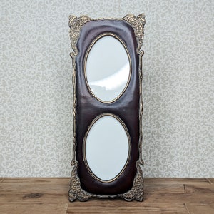 May include: A tall, rectangular double photo frame with a dark brown finish and ornate gold-toned metal detailing at the corners. The frame features two vertical oval openings for photographs, each bordered by a thin gold-colored rim.