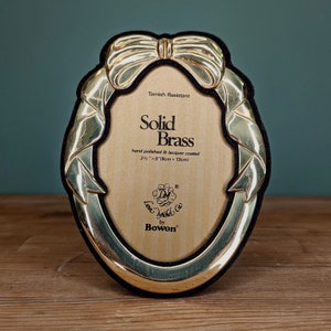 May include: Oval solid brass photo frame with a bow design. The frame is hand polished and lacquer coated, measuring 3.5" x 5" (9cm x 13cm). The frame is tarnish resistant and has the text "Solid Brass".