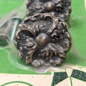 May include: Two ornate silver-toned metal drawer pulls with a floral design. The pulls are packaged in a clear plastic bag.