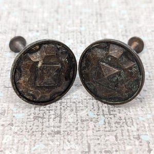 May include: Two antique bronze curtain tiebacks with a geometric design. The tiebacks have a square shape in the center with a raised diamond pattern.