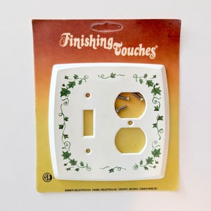 May include: White plastic light switch and outlet cover plate with a green ivy design. The package says "Finishing Touches" and includes screws.