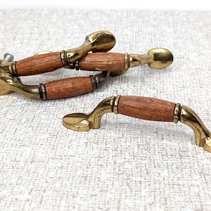 May include: Four vintage cabinet knobs with a wood and brass finish. The knobs have a curved shape and a simple design.