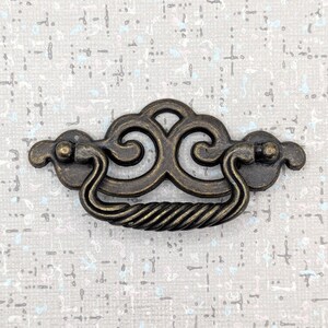 Peut inclure: Poignée de tiroir antique en bronze avec un design décoratif. La poignée présente une poignée incurvée avec une texture de corde torsadée et des détails ornés. La quincaillerie est conçue pour les meubles et les armoires.