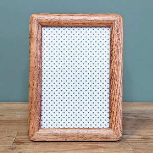 May include: A rectangular wooden picture frame with a light brown finish. The frame holds a white background with a pattern of small, evenly spaced gray polka dots. The frame is displayed on a wooden surface against a teal background.