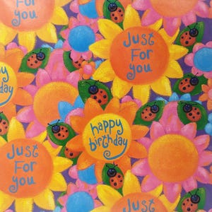 May include: Colorful wrapping paper with a repeating pattern of yellow sunflowers, pink flowers, and red ladybugs. The text "Just For You" and "Happy Birthday" are written on the paper.