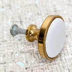 Peut inclure: Un bouton en céramique blanche avec une bordure en métal doré. Le bouton est doté d'une vis pour le fixer à une surface.