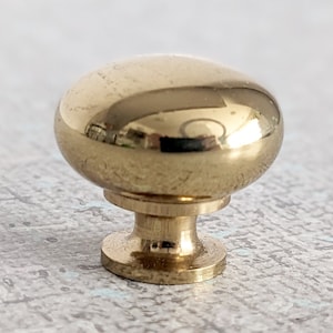 May include: A polished brass cabinet knob with a round top and a short, cylindrical base.