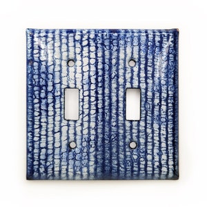 May include: A white and blue ceramic light switch cover with a textured pattern. The cover has two toggle switches.