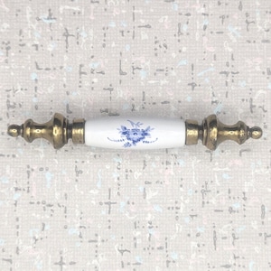 Peut inclure: Une poignée de meuble décorative avec un centre en céramique blanche orné d'un motif floral bleu. Les extrémités sont en métal couleur laiton antique. Convient aux tiroirs et aux armoires.