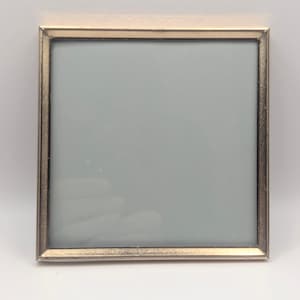 May include: Square silver-toned picture frame with a light blue interior. The frame has a textured border and a simple, elegant design. The frame is empty, ready to display a photograph or artwork.