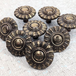 May include: Eight antique brass cabinet knobs with a decorative floral design. Each knob has a raised centre circle and a scalloped edge.