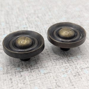 May include: A white ceramic mug with a black handle and the text "But First, Coffee" in a bold, black font. The mug is on a wooden surface. The mug is approximately 10 cm tall.