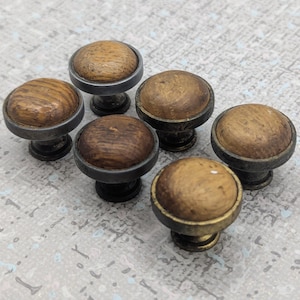 Peut inclure: Six boutons de meubles en bois avec une base en métal foncé. Les boutons ont une forme arrondie et bombée avec un grain de bois visible. La base en métal a une finition sombre et antique. Les boutons sont disposés en cercle.
