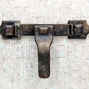 May include: A vintage-style,  metal latch with a t-shaped handle. The latch is  bronze in color and has a worn, aged look.