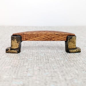 May include: A wooden cabinet pull with a curved top and brass accents. The pull is made of wood with a natural finish and has a distressed look.