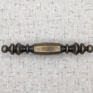 May include: A bronze cabinet pull with an antique finish. The central section is an octagonal shape, with decorative elements and rounded knobs at each end. This handle is suitable for furniture restoration or new builds.