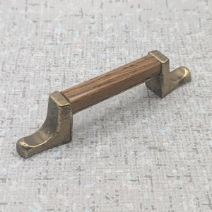 May include: A cabinet pull featuring a light brown wooden handle and antique brass brackets. The brackets have a curved, foot-like shape. This furniture hardware is designed for home decor and cabinets.