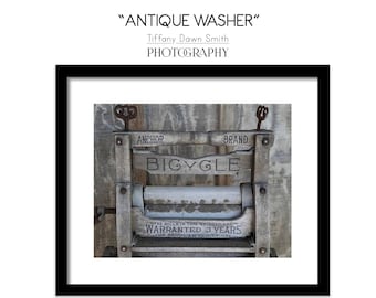 May include: A framed print titled "ANTIQUE WASHER" featuring a vintage wooden washing machine. The machine has the word "BIGYCLE" on it, with "ANCHOR BRAND" above. The print is a Gallery Quality Giclée Fine Art Print.