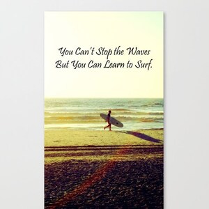 K&ouml;nnte beinhalten: Leinwanddruck mit einer Strandszene, auf der eine Person ein Surfbrett tr&auml;gt. Der Text "You Can't Stop the Waves But You Can Learn to Surf" ist in eleganter Schrift &uuml;ber der Person zu sehen. Das Bild hat einen warmen, goldenen Farbton.