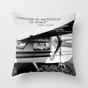 May include: Black and white photograph of a small airplane with the quote "Adventure is worthwhile in itself." - Amelia Earhart printed on top.